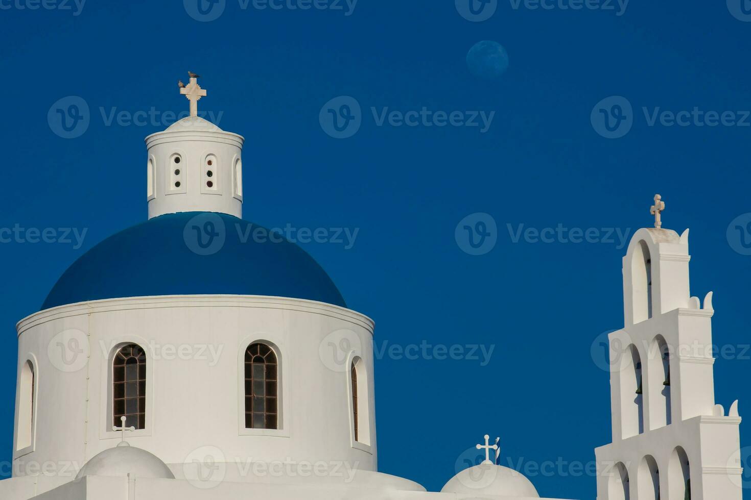 cupola e campana Torre di il Chiesa di panagia platsani e il Luna collocato nel Oia città a santorini isola nel un' bellissimo presto primavera giorno foto