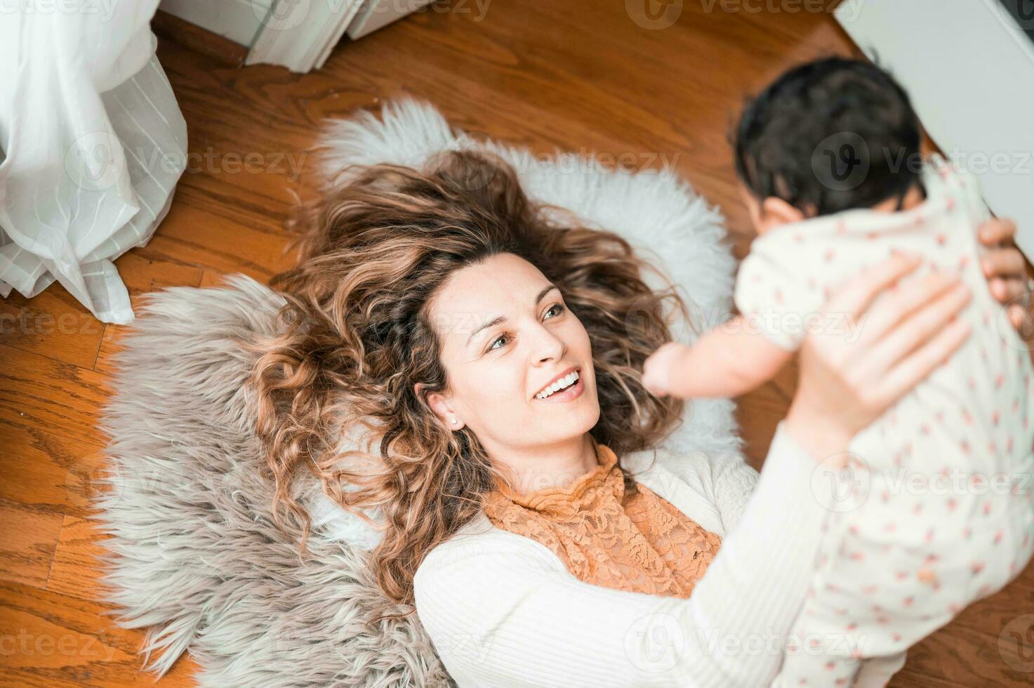 un' donna è Tenere sua bambino mentre posa su il pavimento foto