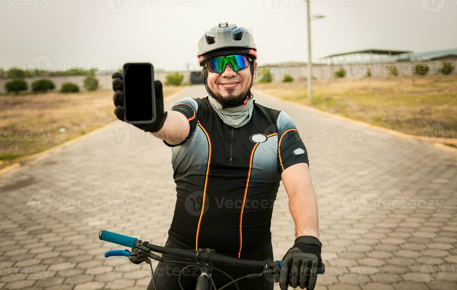 ciclista nel abbigliamento sportivo mostrando il Telefono schermo. maschio ciclista su il bicicletta mostrando cellula Telefono schermo all'aperto. sorridente ciclista mostrando un annuncio pubblicitario su cellula Telefono foto