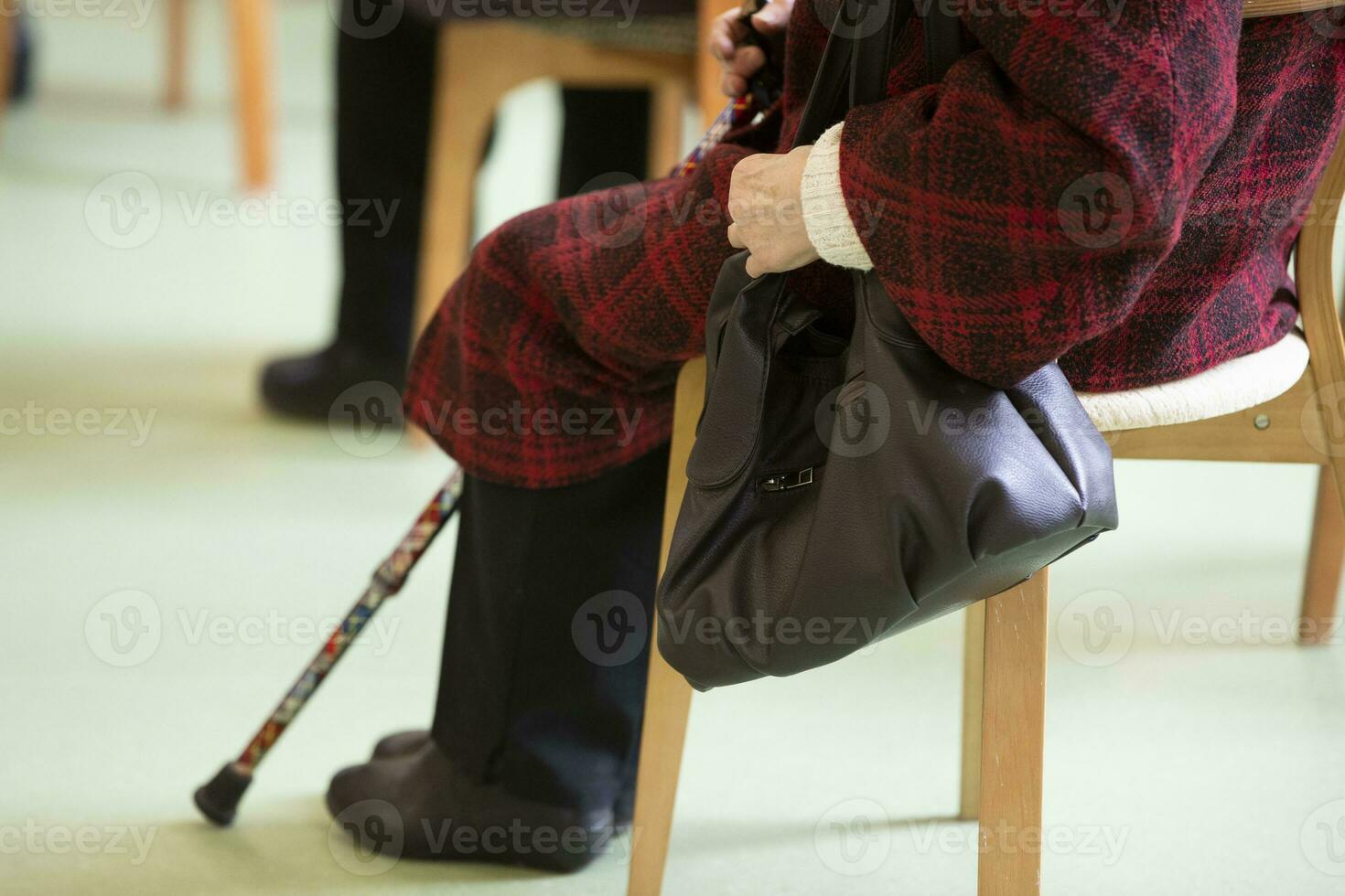 un vecchio donna è seduta su un' sedia con un' bastone. vecchio età è non un' la gioia. foto