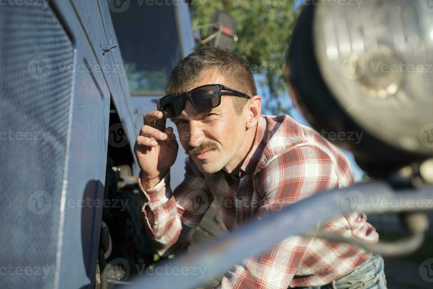 divertente nazione uomo riparazione un' trattore. il uomo nel un' camicia nel un' gabbia è un' macchina operatore. foto