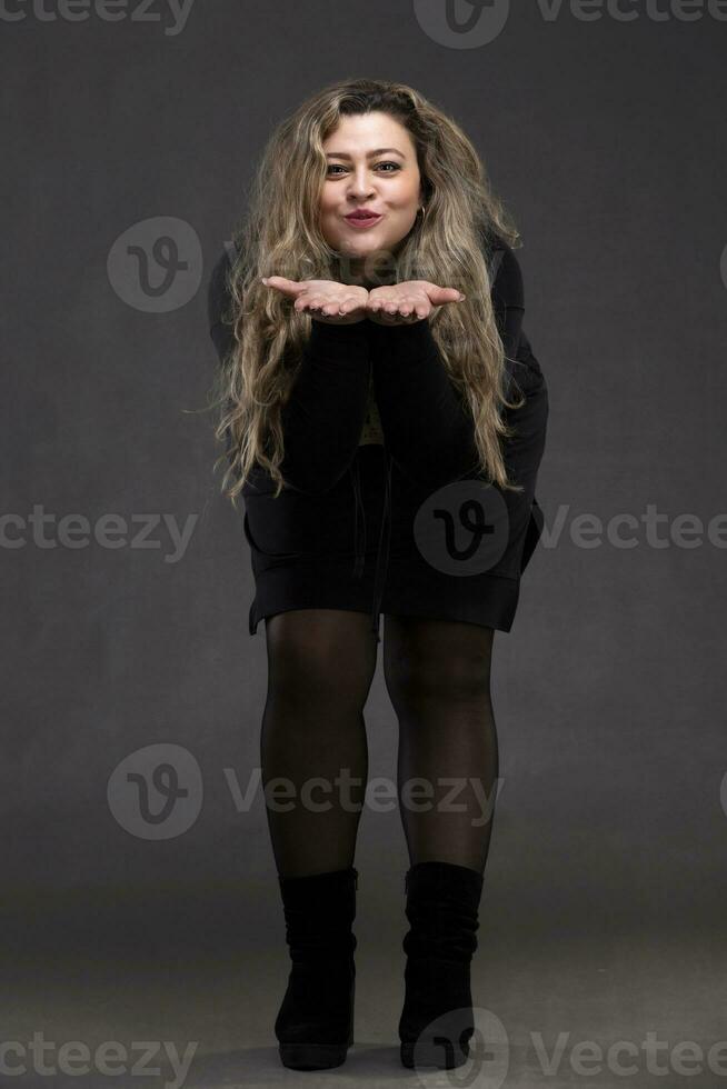 bellissimo Grasso donna con lungo Riccio capelli e nero vestito soffiaggio su sua braccia. foto