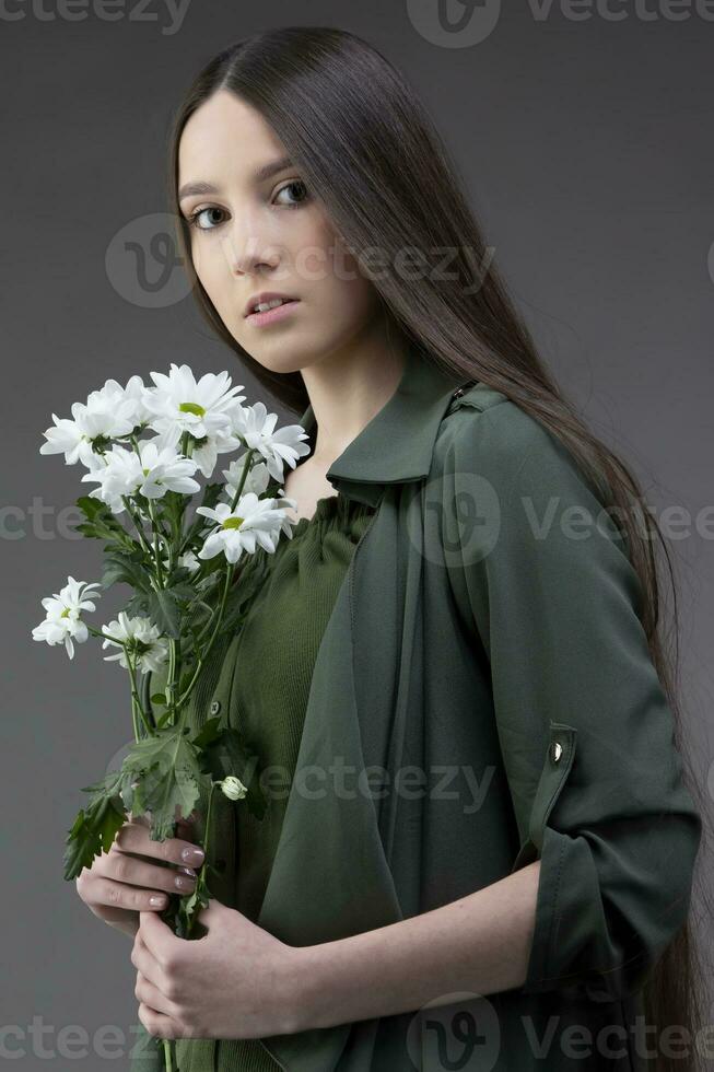 un' bellissimo giovane ragazza con naturale bellezza con lungo liscio capelli detiene un' mazzo di bianca crisantemi. foto