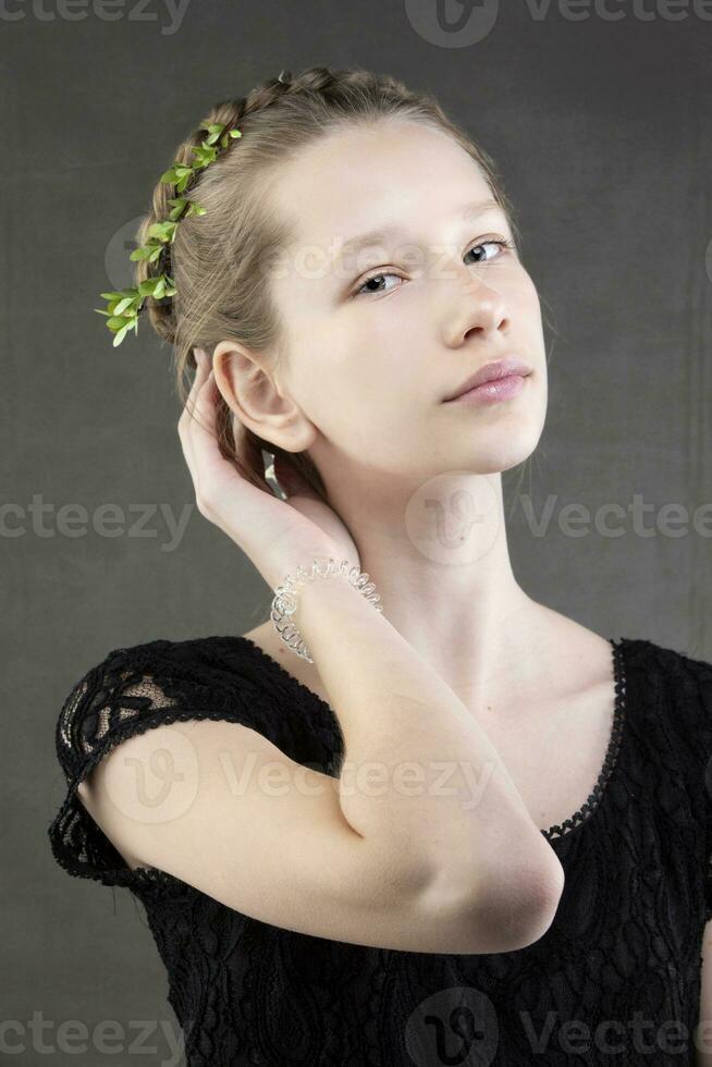 un' bellissimo adolescenziale ragazza con un' treccia con un' verde ramoscello di un' albero intrecciata in esso su un' grigio sfondo. ritratto di un' premuto ragazza con sofisticato caratteristiche. foto