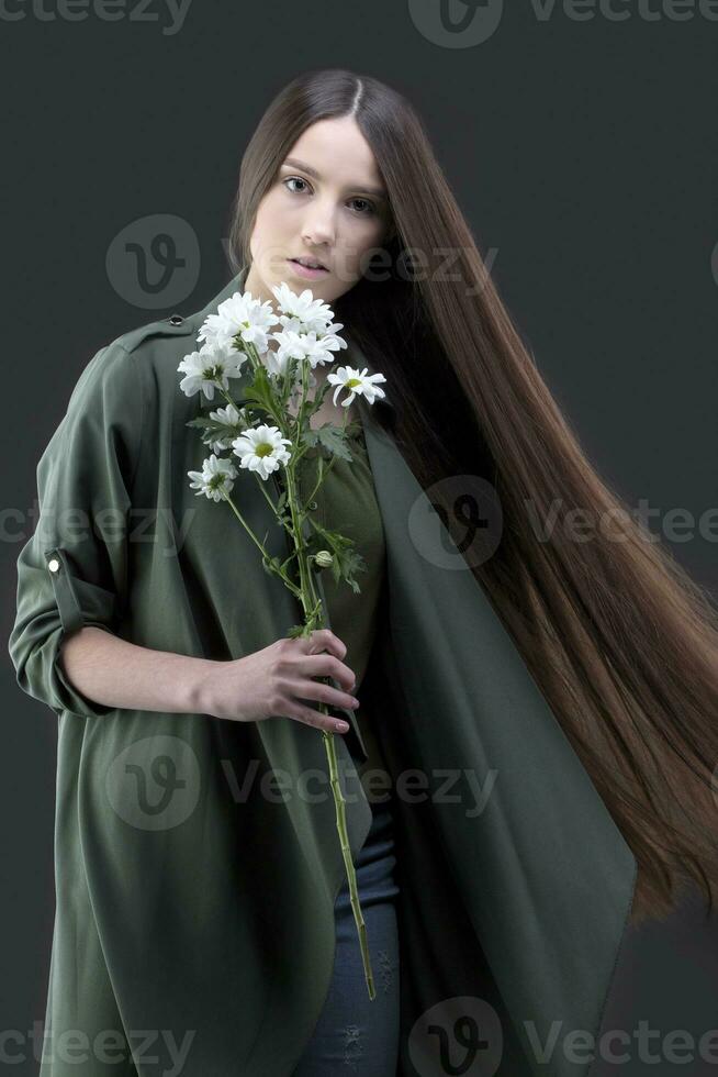 un' bellissimo giovane ragazza con naturale bellezza con lungo liscio capelli detiene un' mazzo di bianca crisantemi. foto