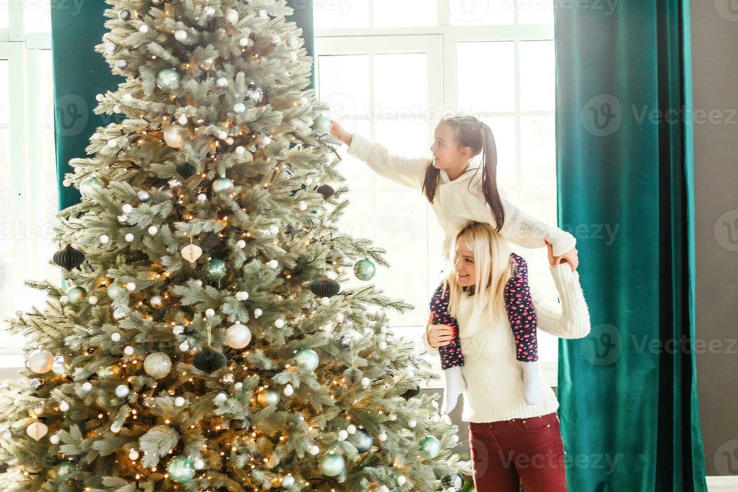 contento famiglia donna madre e poco ragazza rilassare giocando sparkler vicino Natale albero su Natale vigilia a casa. mamma, figlia nel Casa con inverno decorazione. Natale nuovo anno tempo per celebrazione foto