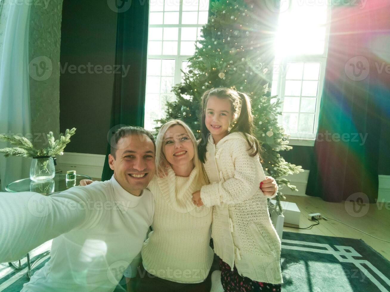 famiglia, vacanze, tecnologia e persone - sorridente madre, padre e poco ragazza fabbricazione autoscatto con telecamera al di sopra di vivente camera e Natale albero sfondo foto