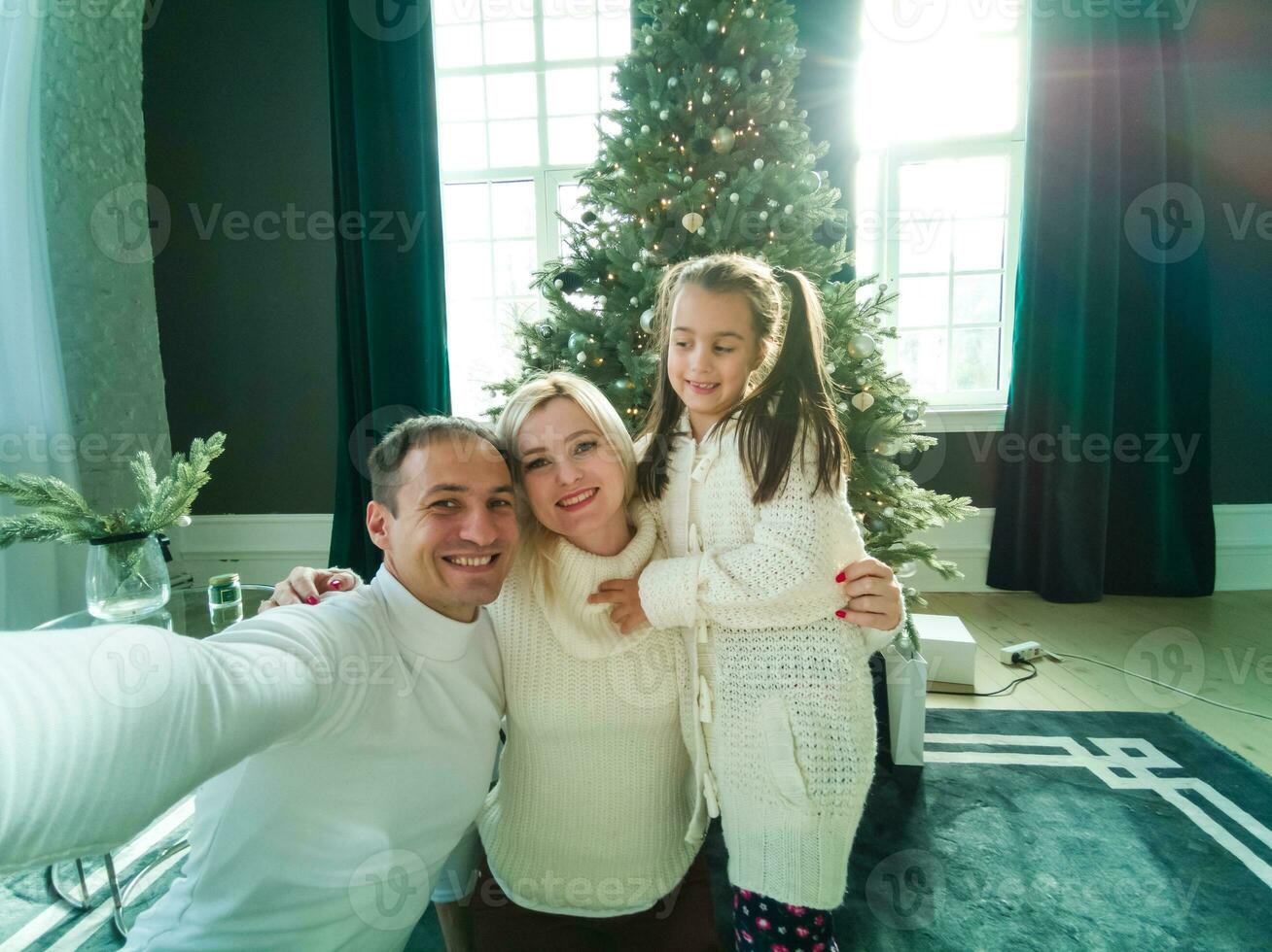 famiglia, vacanze, tecnologia e persone - sorridente madre, padre e poco ragazza fabbricazione autoscatto con telecamera al di sopra di vivente camera e Natale albero sfondo foto