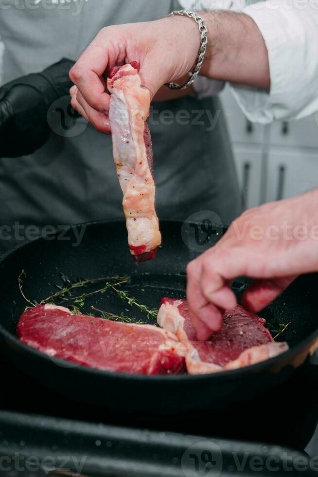 cucinando bistecche nel un' padella. cucinando Manzo a il culinario maestro classe. il mani di il capocuoco nel nero guanti. foto