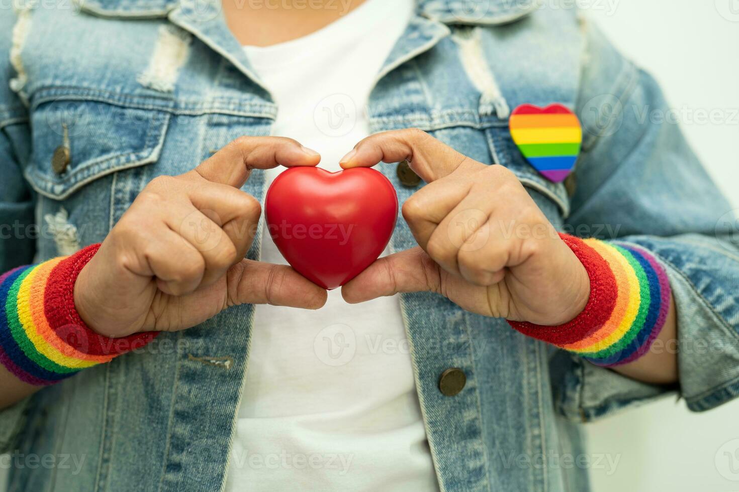 la signora asiatica che indossa braccialetti con bandiera arcobaleno e tiene il cuore rosso, simbolo del mese dell'orgoglio lgbt celebra l'annuale a giugno sociale di gay, lesbiche, bisessuali, transgender, diritti umani. foto