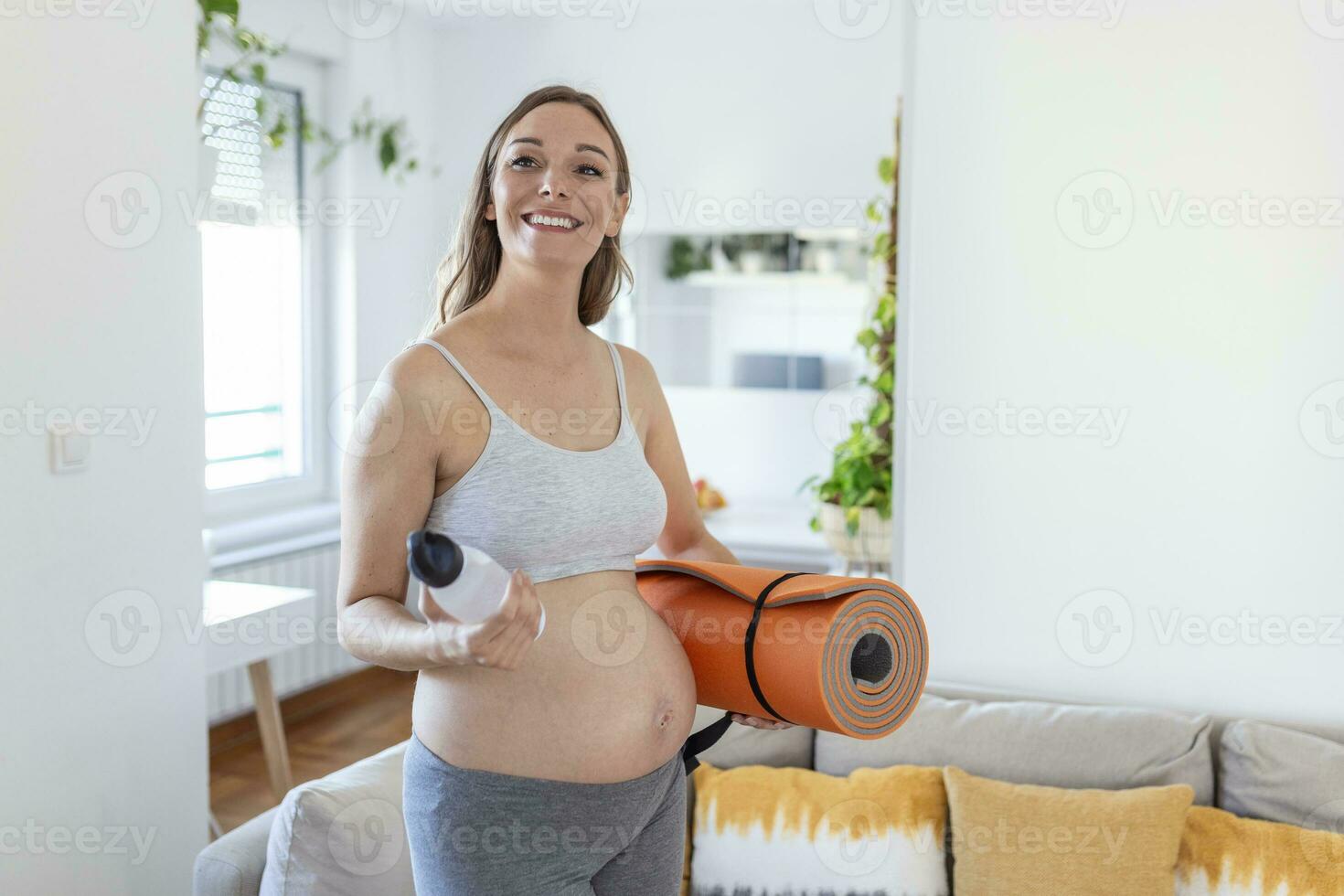 ritagliata tiro sezione centrale di incinta donna Tenere un' yoga stuoia e un' riutilizzabile acqua bottiglia, ottenere pronto per esercizio a casa. benessere. soggiorno in forma e salutare durante gravidanza foto