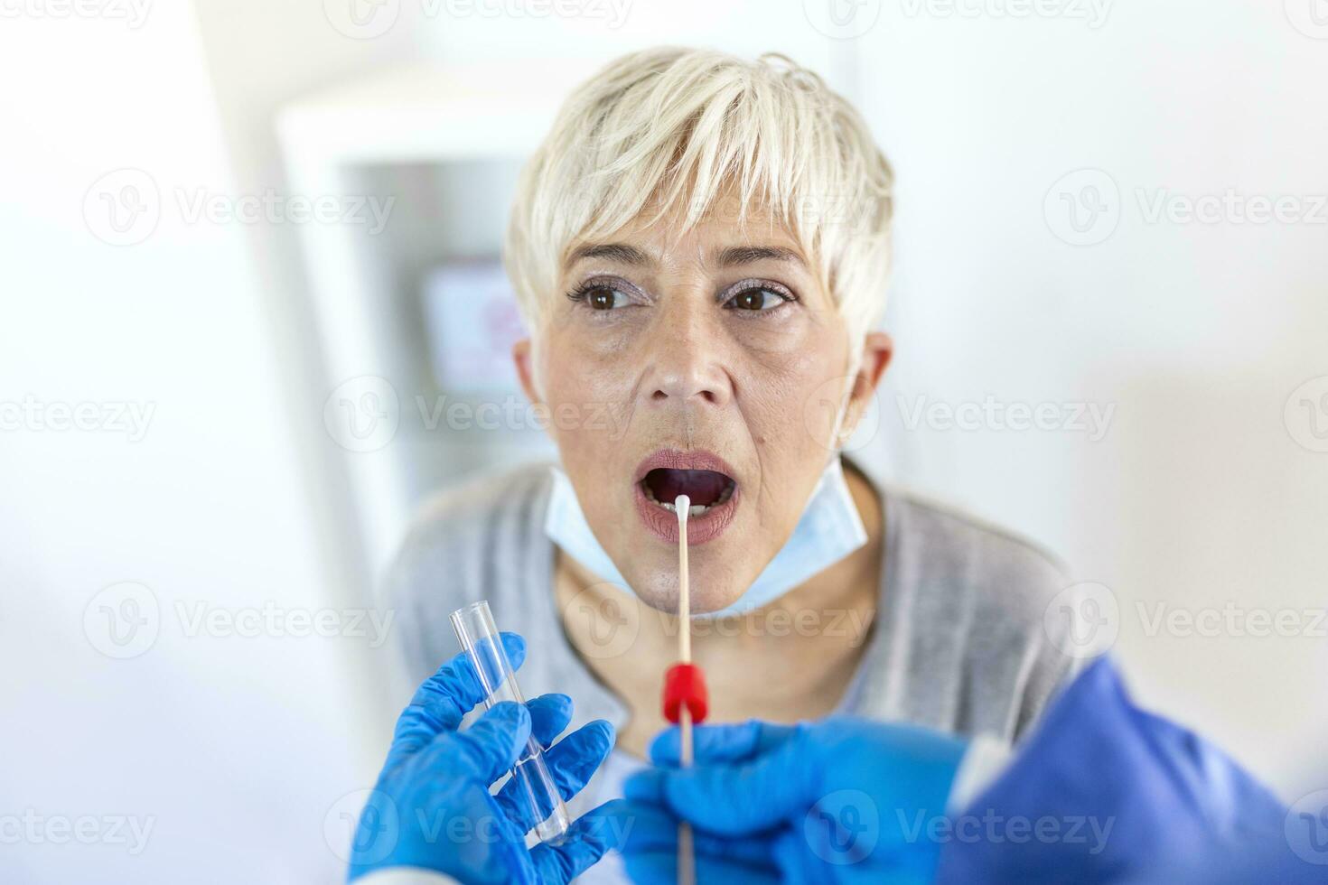 maturo caucasico donna nel un' clinico ambientazione essere tamponato di un' assistenza sanitaria lavoratore nel protettivo abbigliamento per determinare Se lei ha contratto il coronavirus o covid19. foto