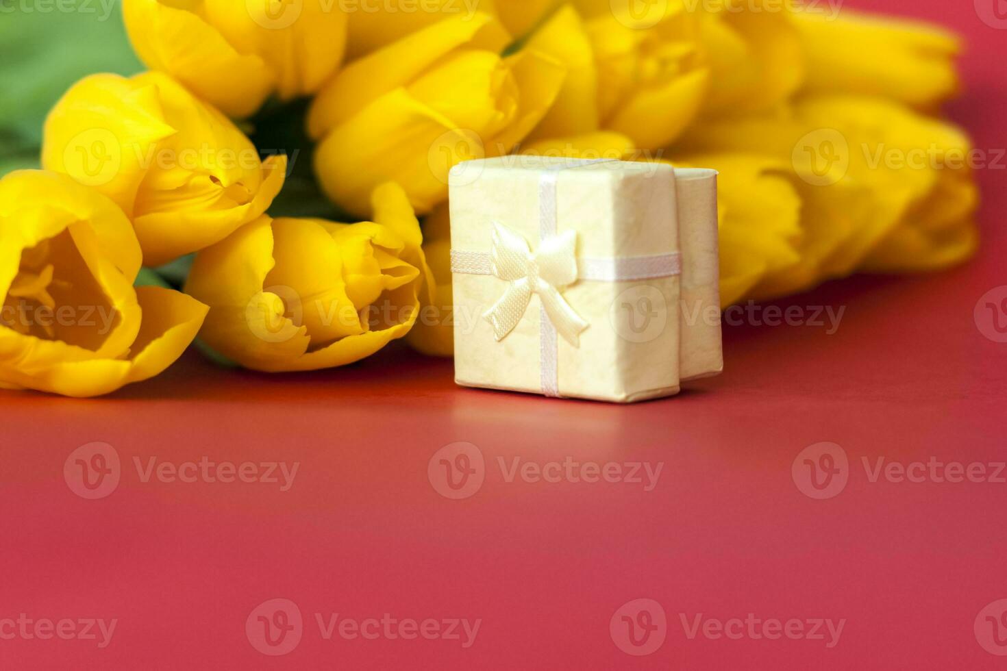 un' mazzo di fresco giallo tulipani su un' rosso sfondo. un' piccolo regalo scatola Il prossimo per il tulipani. primavera fiori. il concetto di primavera o vacanza, marzo 8, internazionale Da donna giorno, foto