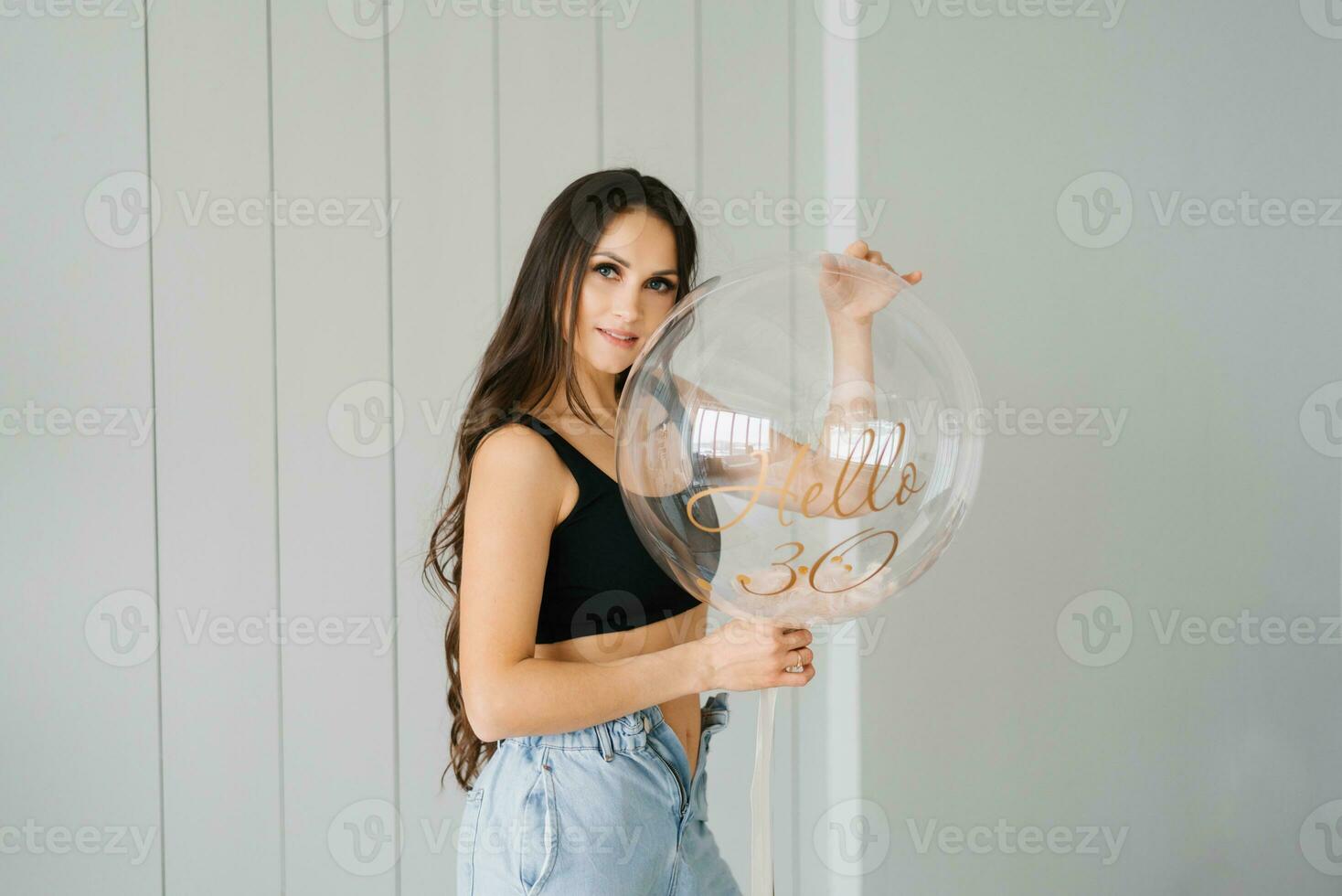 elegante bellissimo giovane caucasico donna con lungo capelli nel un' nero superiore e jeans detiene un' compleanno ballon nel onore di sua trentesimo compleanno foto