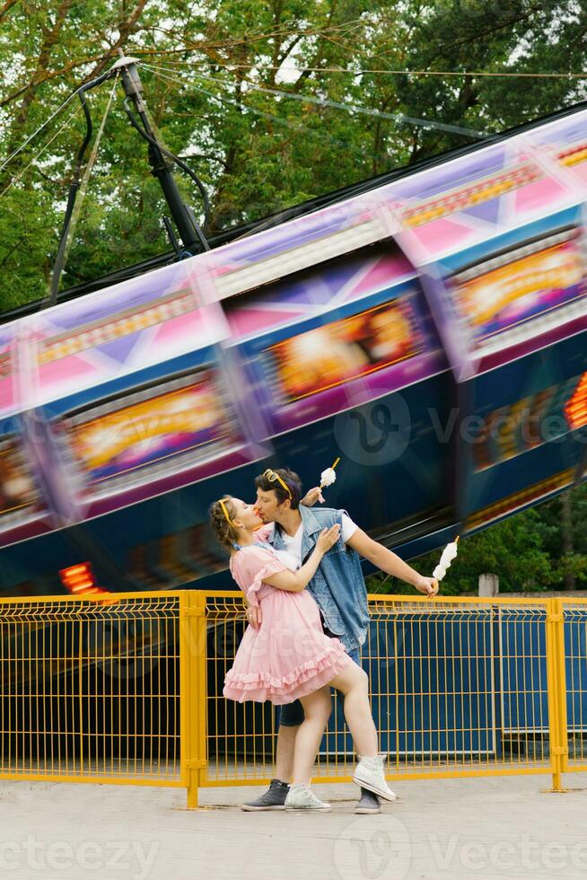 contento coppia nel amore godendo ogni altro nel un divertimento parco. un' tipo e un' ragazza mangiare cotone caramella e ridendo foto