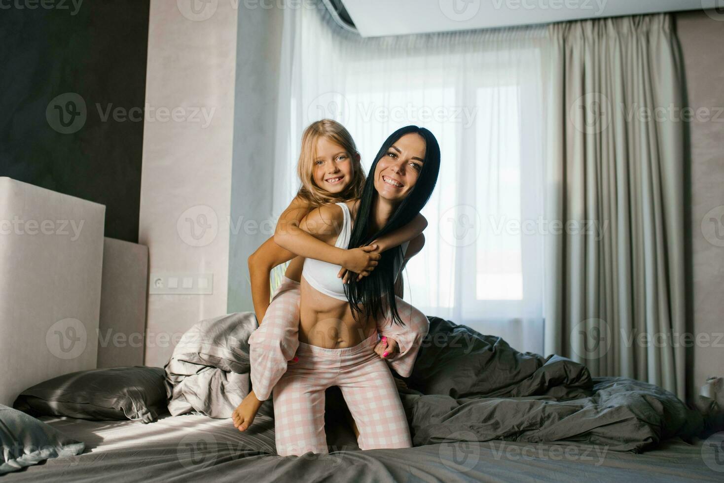 contento mamma e figlia ridere e avere divertimento su il letto nel il mattina foto
