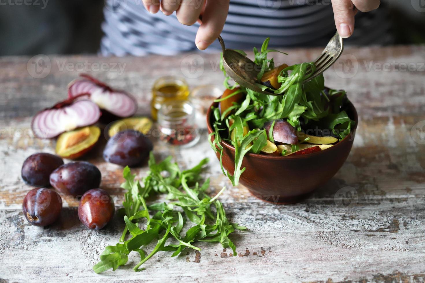 insalata sana mescolare le mani maschili con un cucchiaio e una forchetta. insalata di rucola e prugne. foto