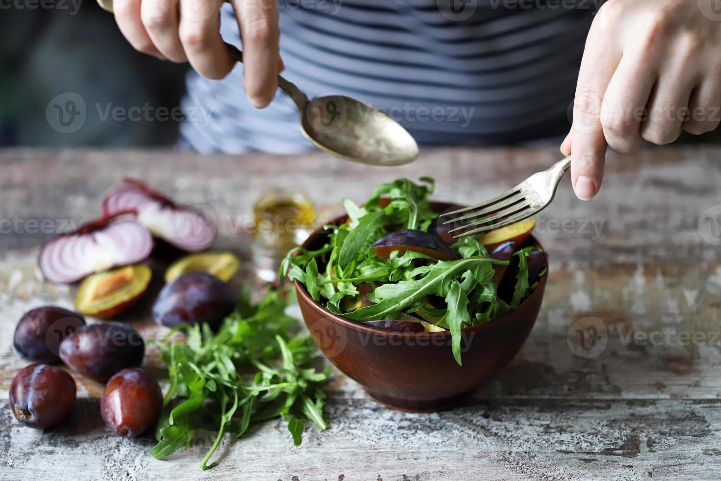 insalata sana mescolare le mani maschili con un cucchiaio e una forchetta. insalata di rucola e prugne. foto