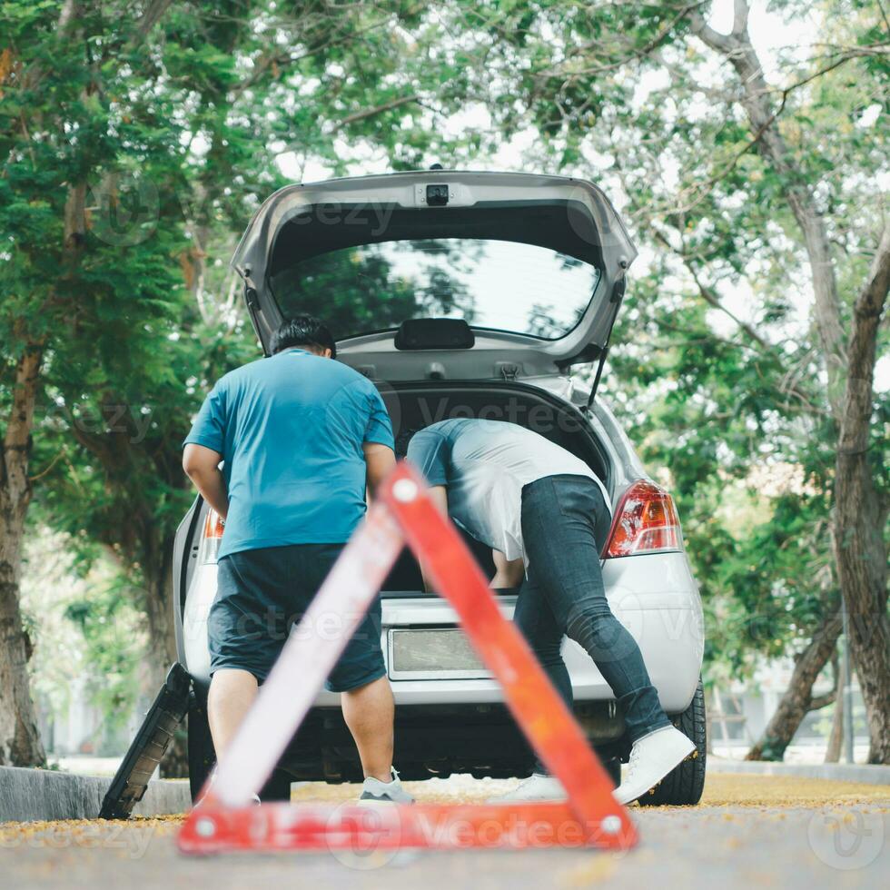 l'uomo asiatico trova strumenti in macchina per la riparazione dell'auto dopo un guasto all'auto in strada. concetto di problema al motore del veicolo o incidente e aiuto di emergenza da un meccanico professionista foto