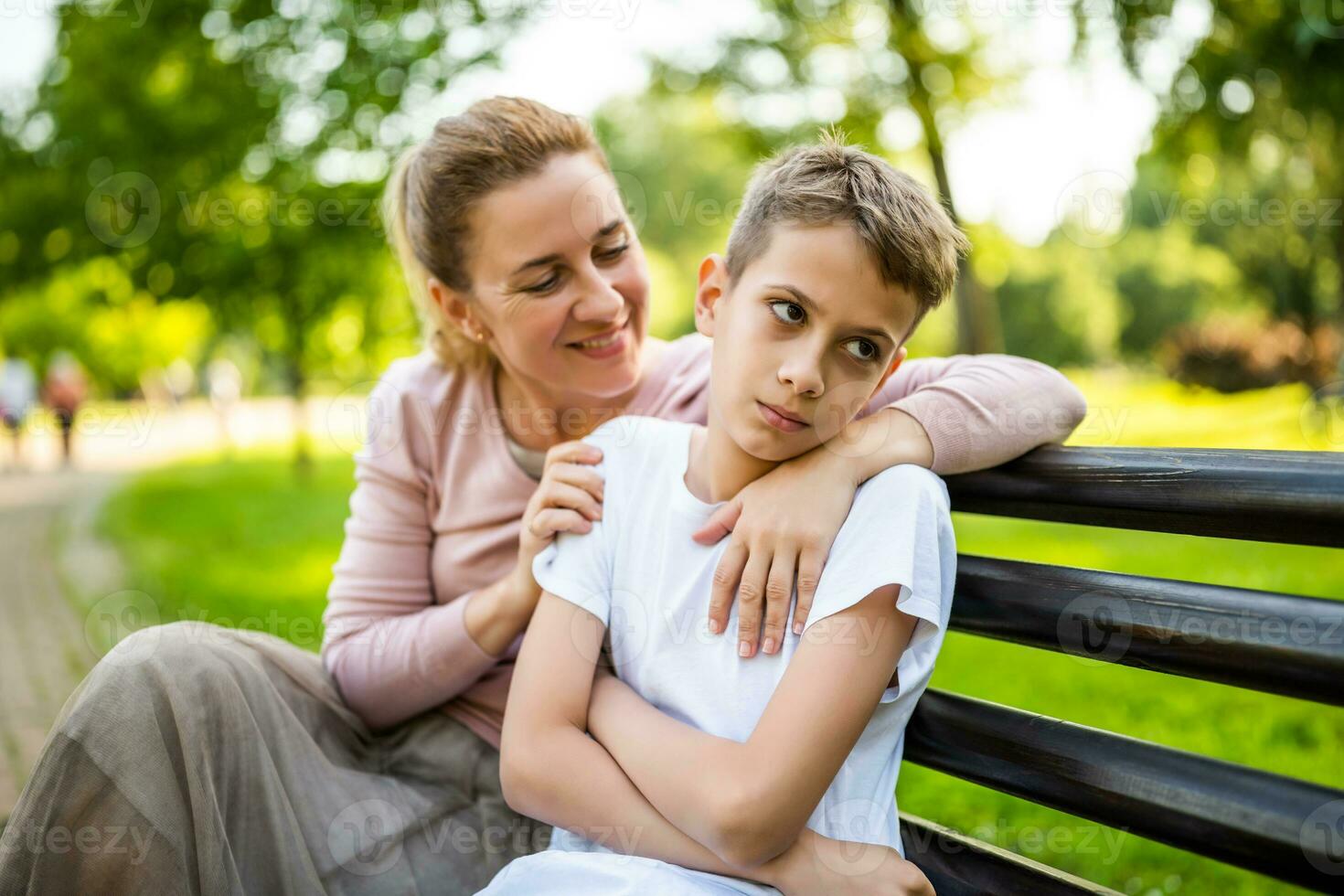 contento madre è seduta con sua figlio su panchina nel parco. ragazzo è offeso e imbronciato. foto