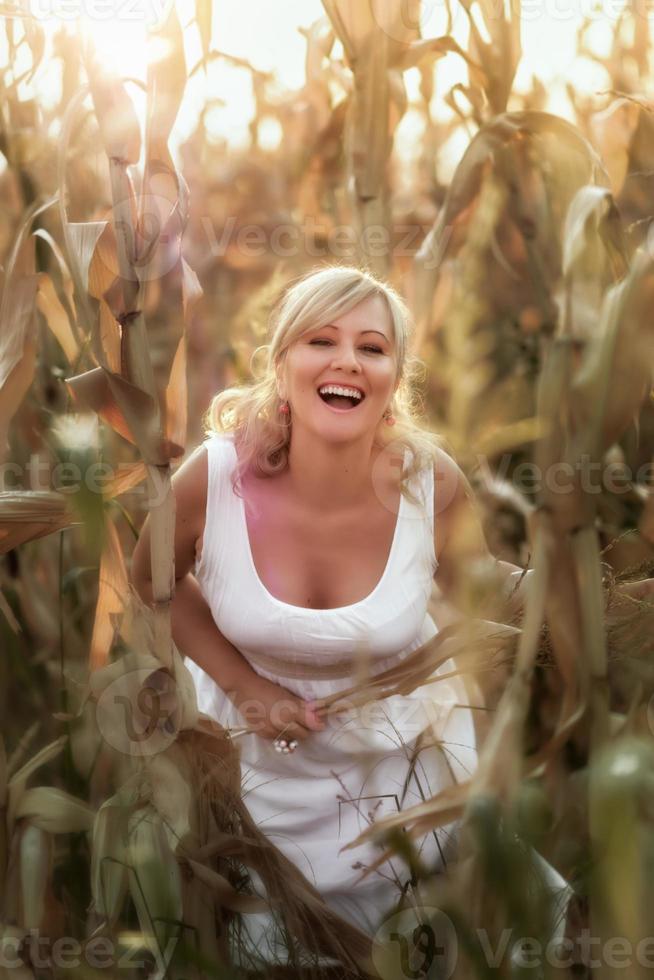 donna in un abito lungo estivo bianco cammina su un campo di grano e posa nell'ora del tramonto. foto