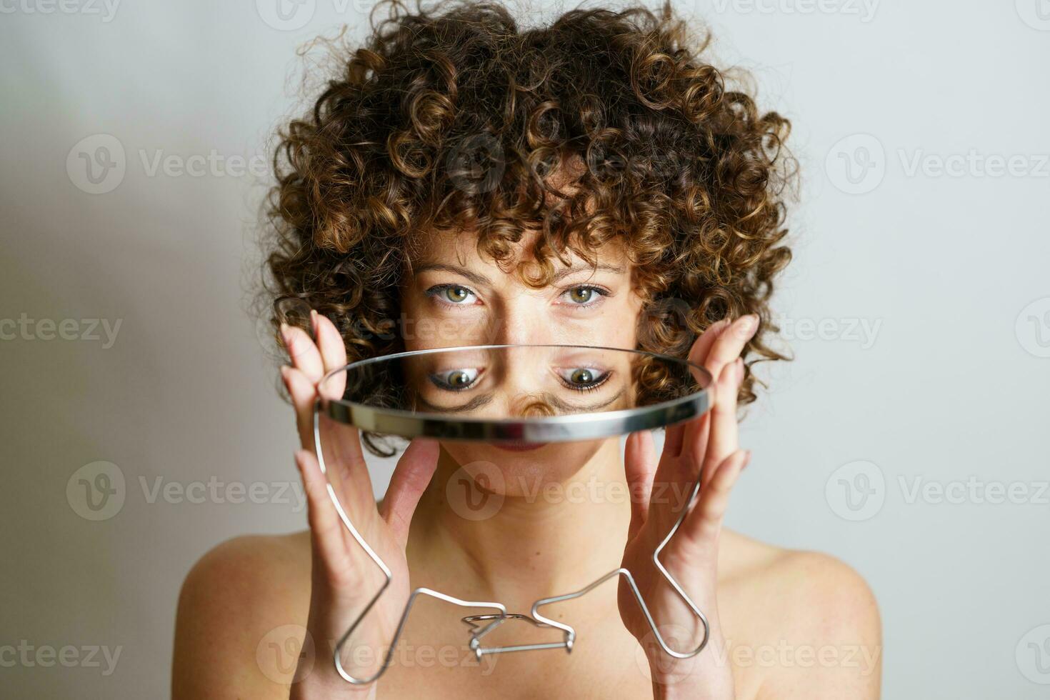 ragazza con Riccio capelli Tenere specchio nel mani con riflessione di occhi foto