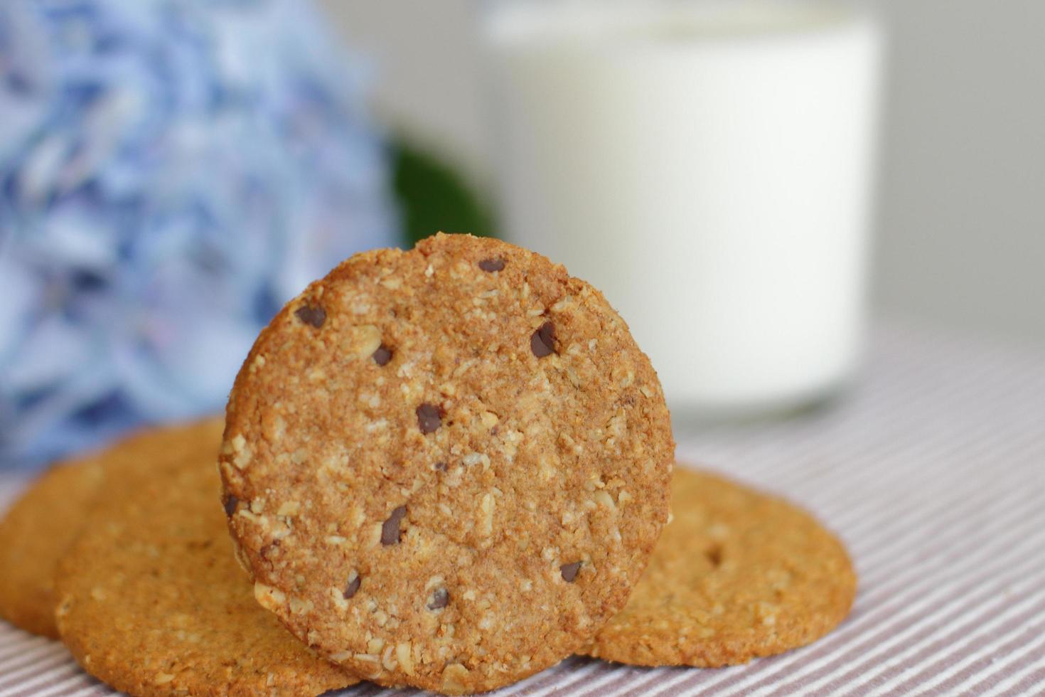 biscotti di avena con bicchiere di latte per colazione su tovaglia e fiore blu sullo sfondo, cibo sano rustico foto