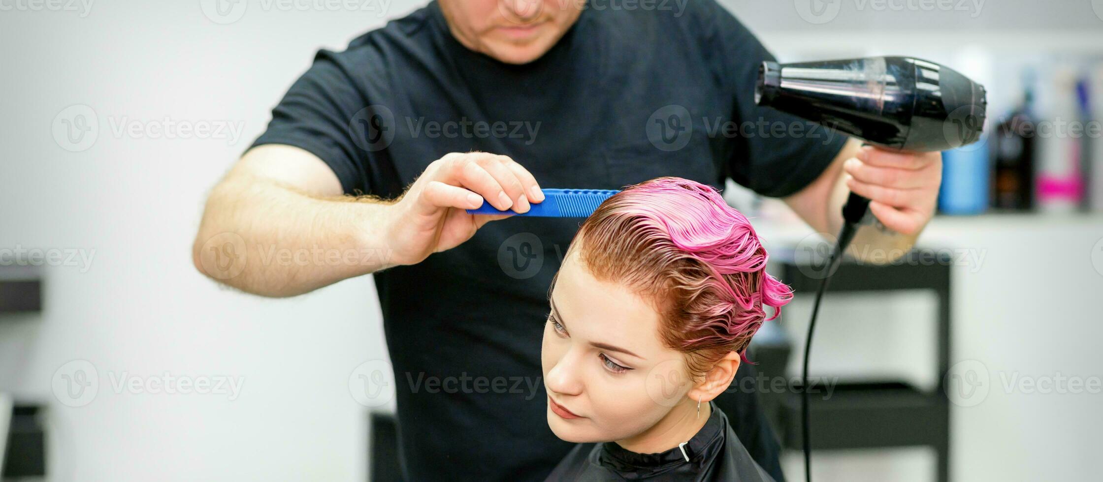 un' parrucchiere è essiccazione il rosa capelli di il giovane donna nel un' bellezza salone. foto