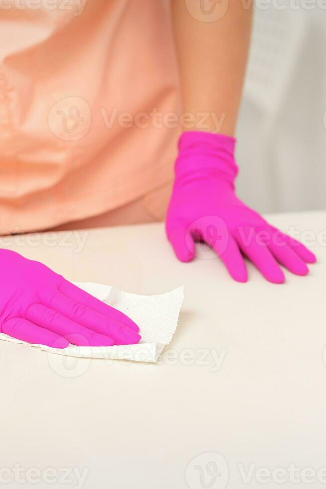vicino su di mani nel gomma da cancellare protettivo rosa guanti pulizia il bianca superficie con un' bianca straccio. foto