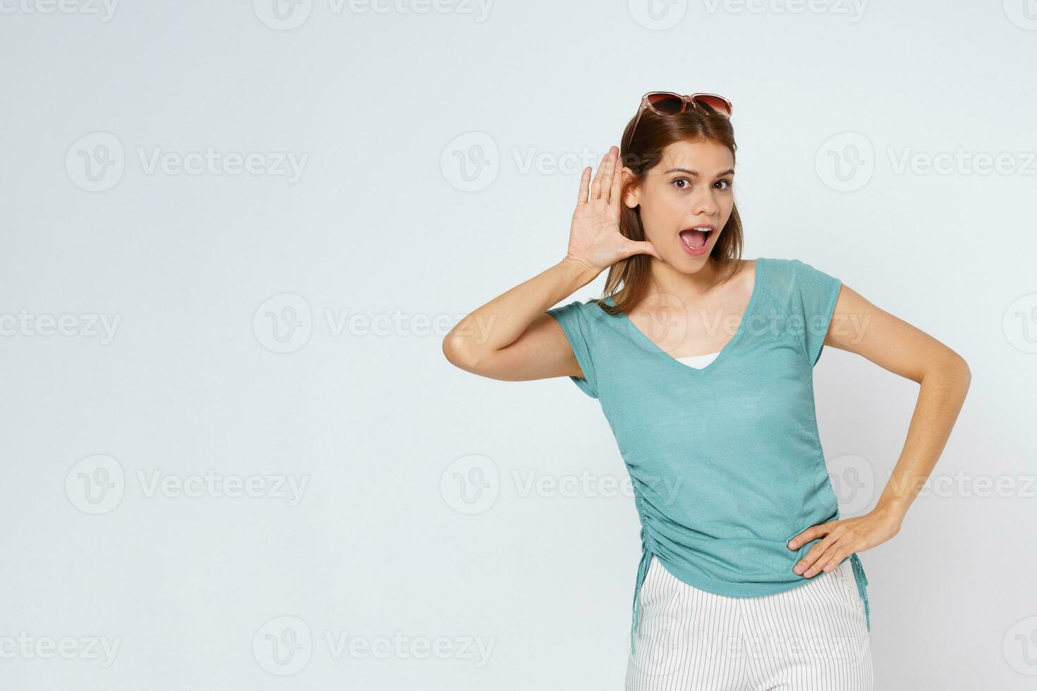 ritratto di giovane donna con ha aperto bocca provando per sentire qualcosa con sollevato mano vicino sua orecchio e guardare a telecamera, mentre in piedi al di sopra di bianca isolato sfondo. foto
