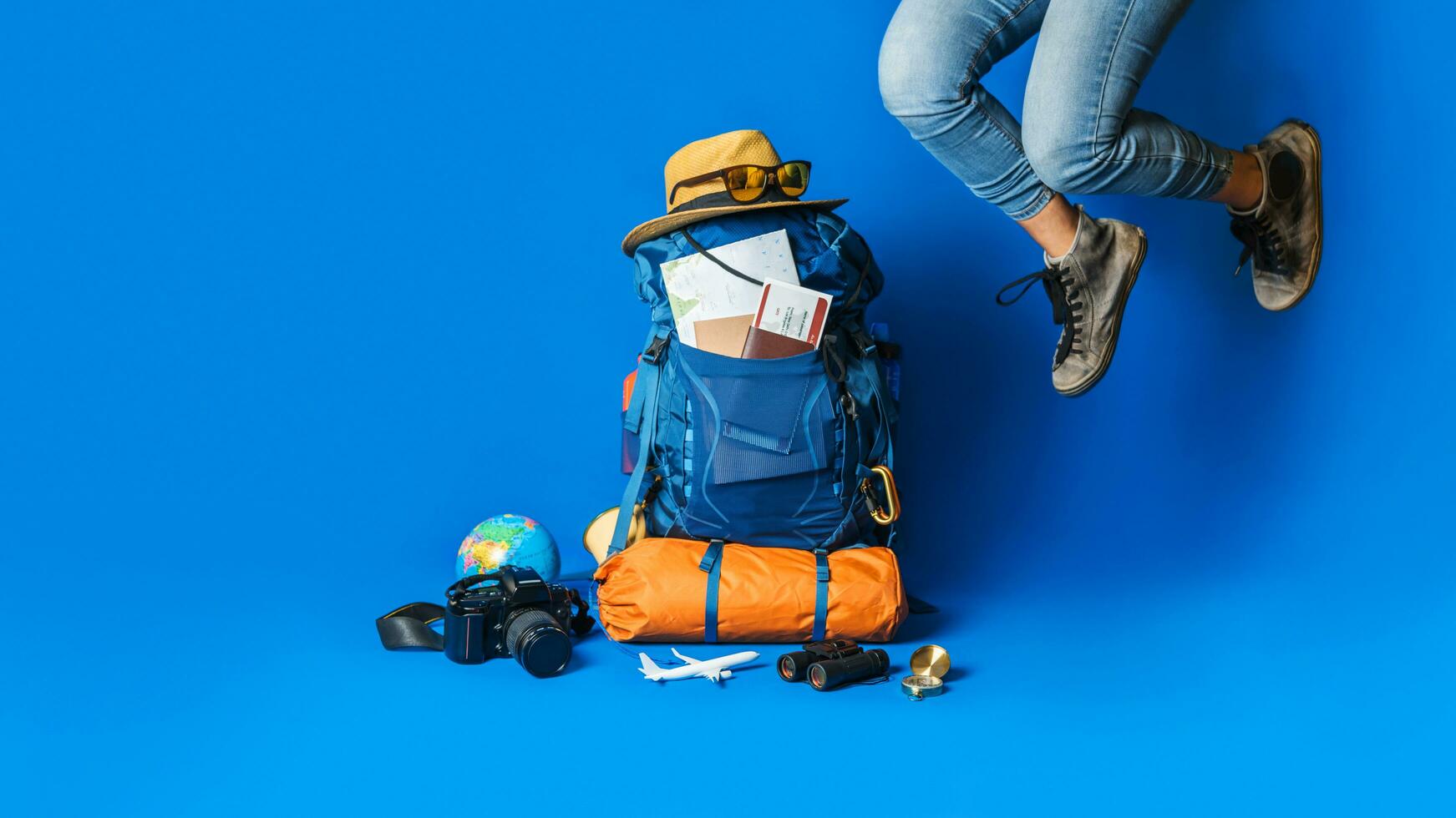 pianificazione turistica vacanza con l'aiuto della mappa del mondo con altri accessori da viaggio in giro. donna che viaggia con la valigia su sfondo di colore blu. zaino da viaggio concept foto