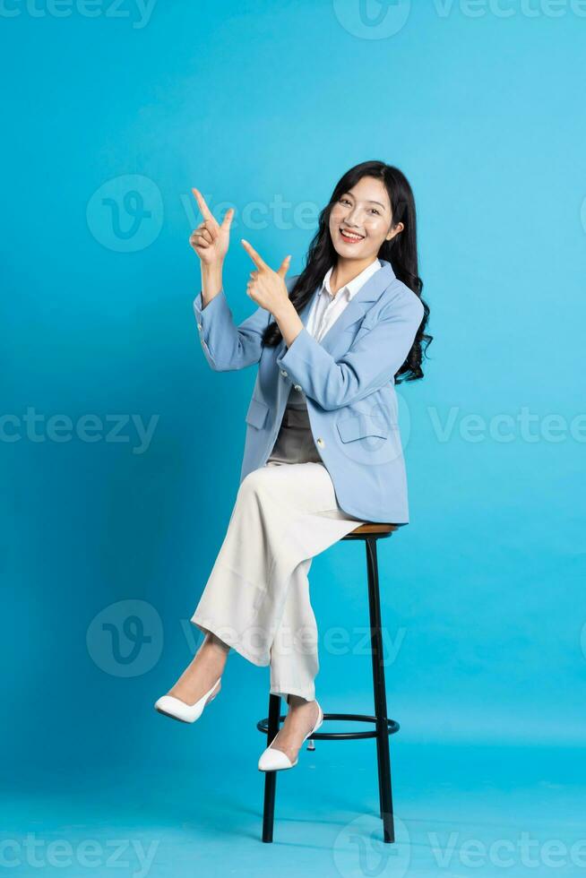 asiatico donna d'affari ritratto seduta su sedia, isolato su blu sfondo foto