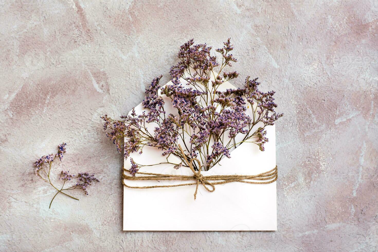un' mazzo di secco fiori nel un' leggero Busta legato con un' corda su un' strutturato sfondo. saluto romantico carta. superiore Visualizza foto
