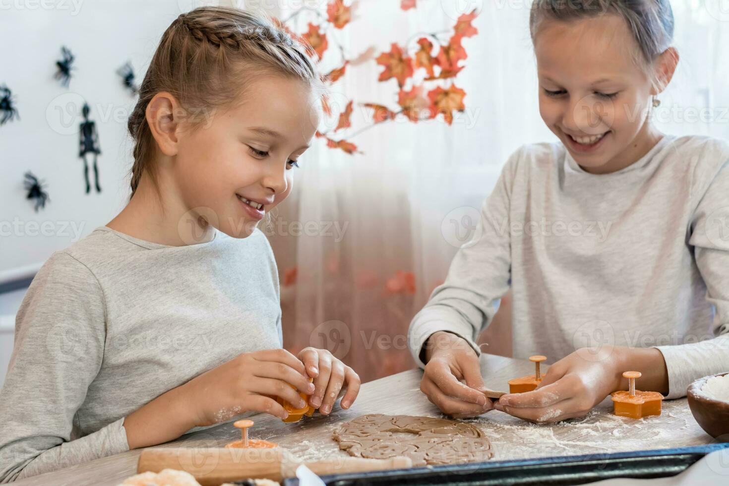 preparazione per celebrare Halloween e preparazione un' trattare. bello ragazze siamo guardare a ritagliare Halloween biscotti a partire dal Impasto e sorridente nel il casa cucina. stile di vita foto