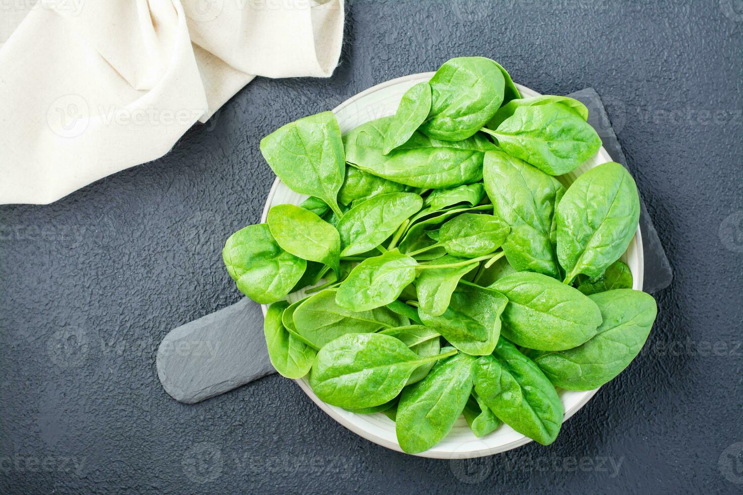 fresco bambino spinaci le foglie nel gocce di acqua su un' piatto su un' ardesia tavola su un' nero sfondo. vegetariano, benessere e disintossicazione cibo. superiore Visualizza foto