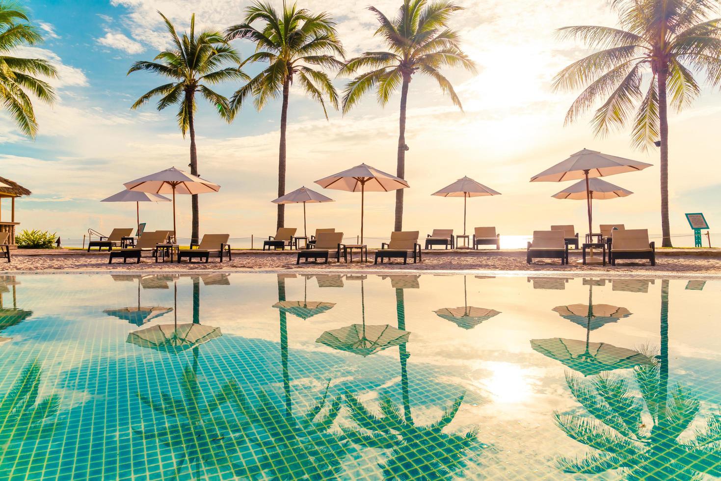 bellissimo ombrellone di lusso e sedia intorno alla piscina all'aperto in hotel e resort con palme da cocco al tramonto o all'alba sky foto