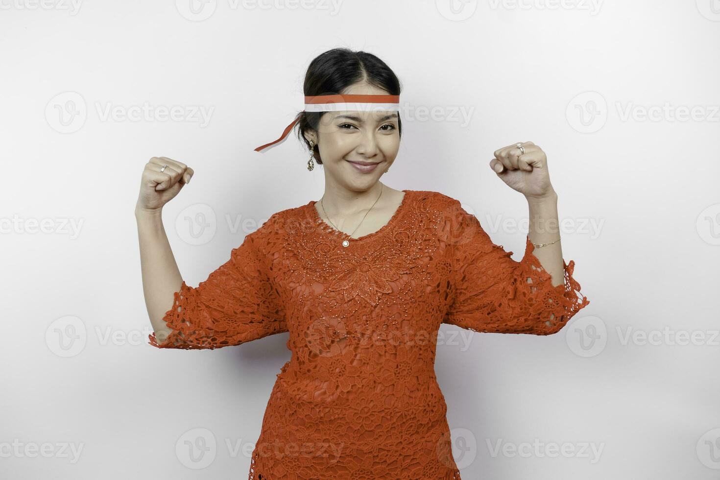 eccitato asiatico donna indossare un' rosso kebaya e fascia per capelli mostrando forte gesto di sollevamento sua braccia e muscoli sorridente con orgoglio. dell'Indonesia indipendenza giorno concetto. foto