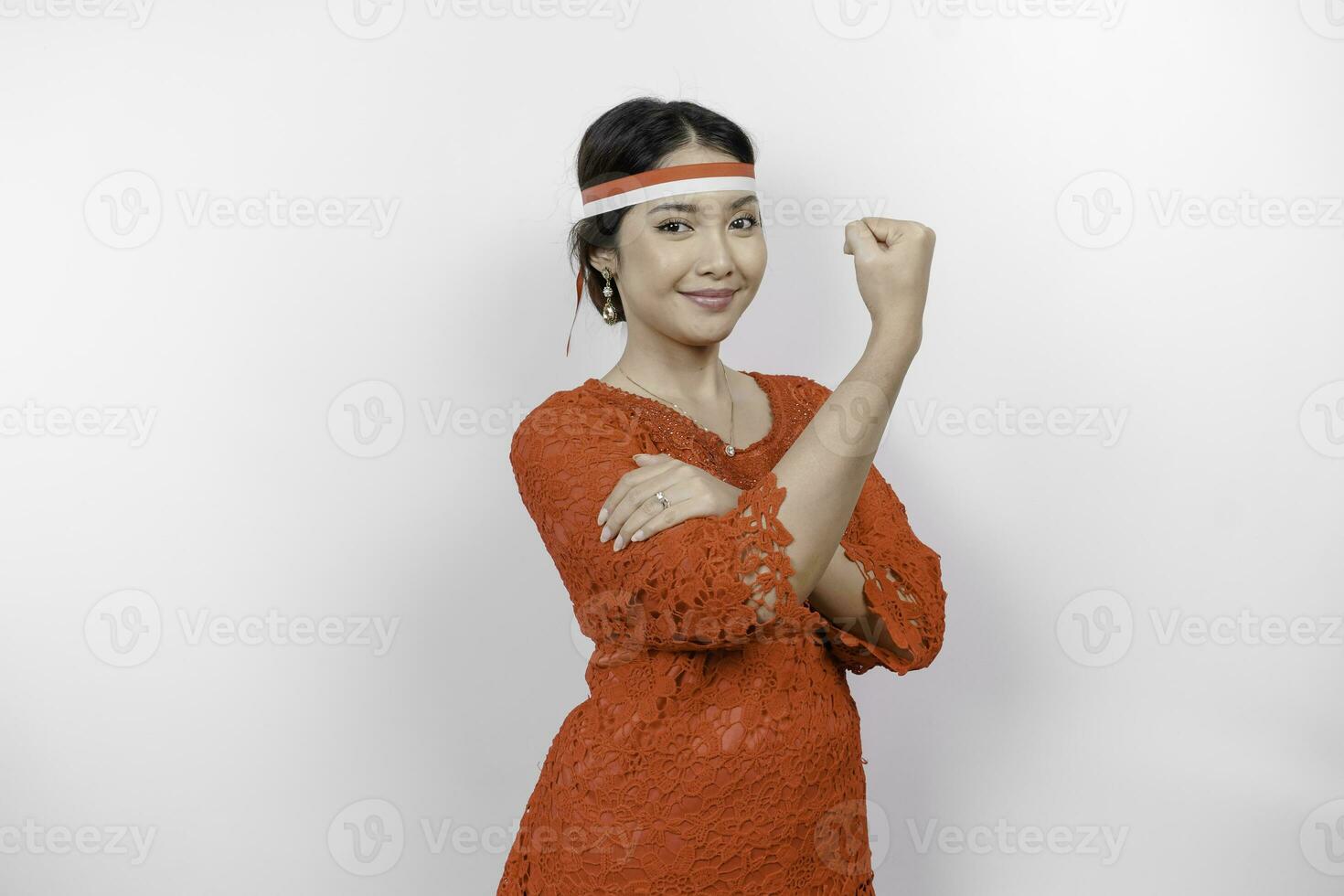 eccitato asiatico donna indossare un' rosso kebaya e fascia per capelli mostrando forte gesto di sollevamento sua braccia e muscoli sorridente con orgoglio. dell'Indonesia indipendenza giorno concetto. foto