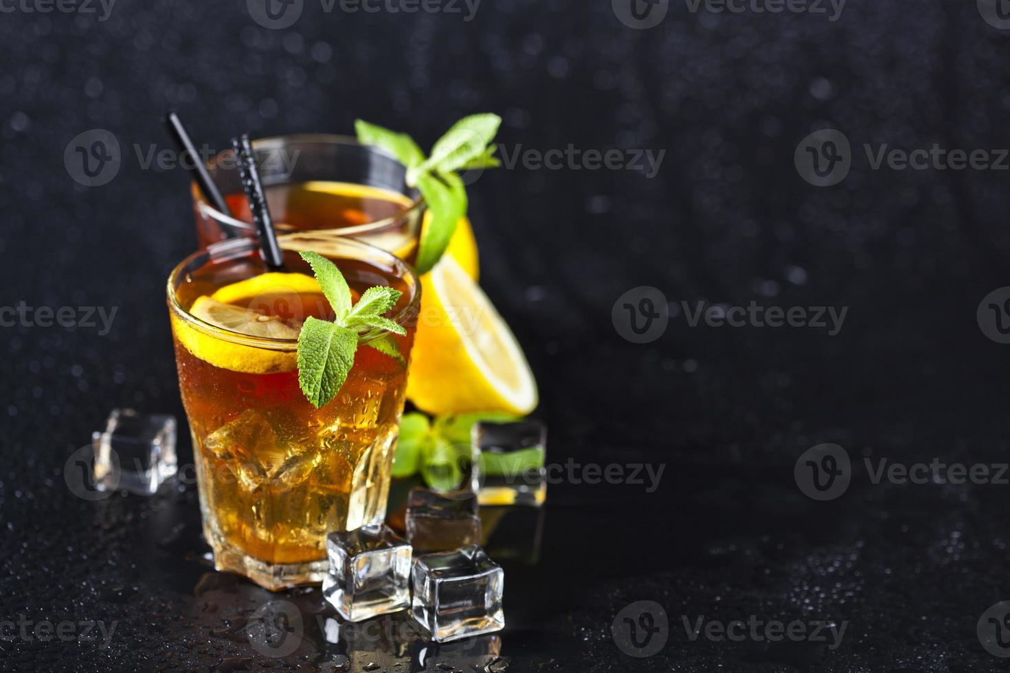 tè freddo tradizionale con limone, foglie di menta e cubetti di ghiaccio in due bicchieri su sfondo nero bagnato. foto