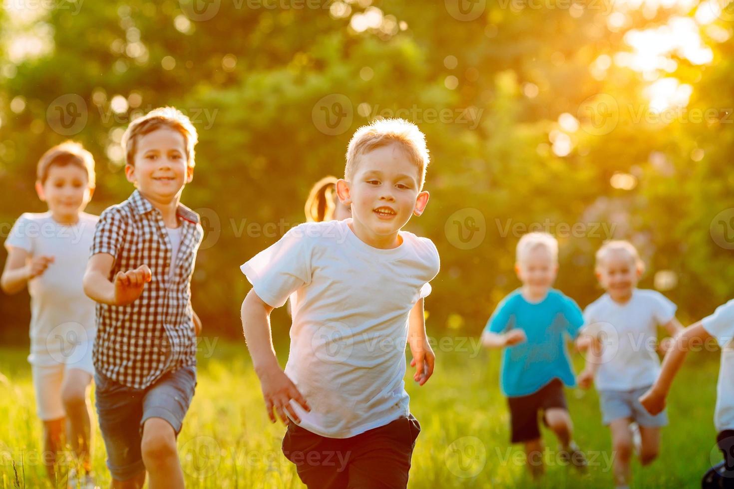 un gruppo di bambini felici di ragazzi e ragazze corrono nel parco sull'erba in una soleggiata giornata estiva. foto