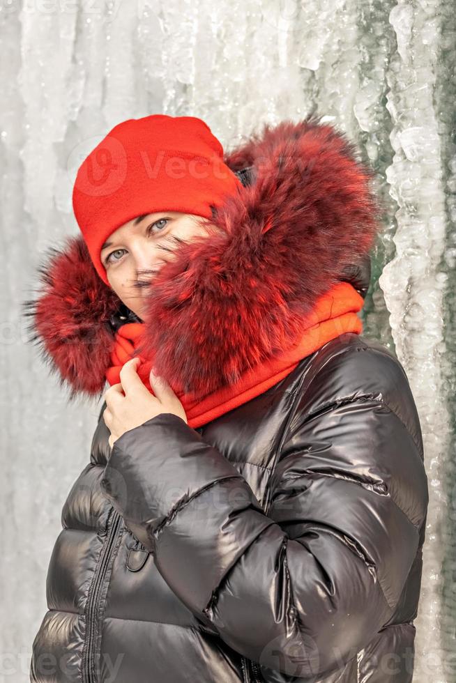 ritratto di una donna con cappello e sciarpa rossi, giacca calda sullo sfondo di un muro di ghiaccio. inverno foto