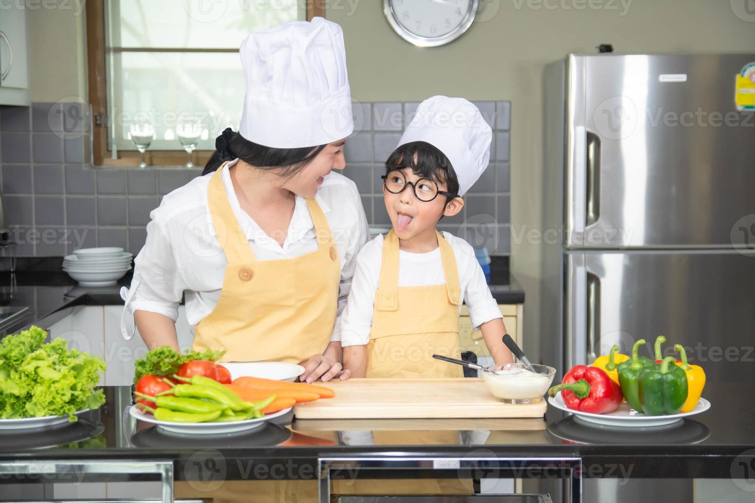 donna asiatica giovane madre con figlio ragazzo cucina insalata cibo con verdure tenendo pomodori e carote, peperoni sul piatto per famiglia felice cucinare cibo godimento stile di vita cucina in casa foto