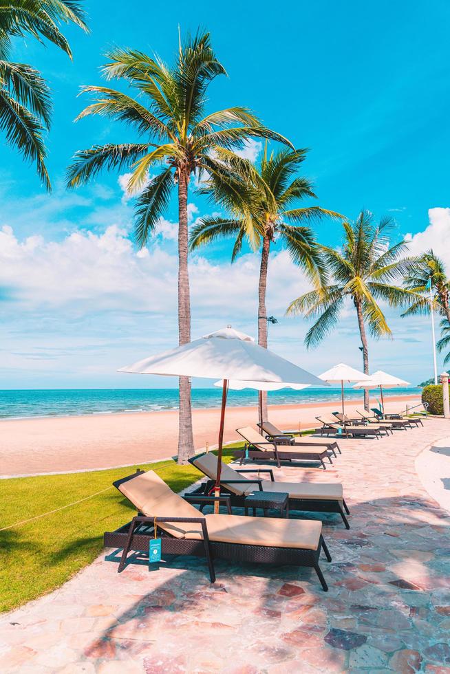 bellissima spiaggia tropicale e mare con ombrellone e sedia intorno alla piscina nel resort dell'hotel foto