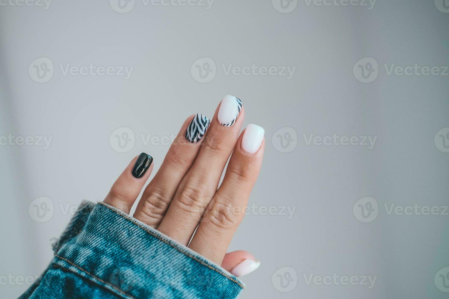 bellissimo femmina mani con un' manicure nel un' denim giacca. elegante chiodo design. manicure con nero e bianca zebra strisce su il chiodo. foto