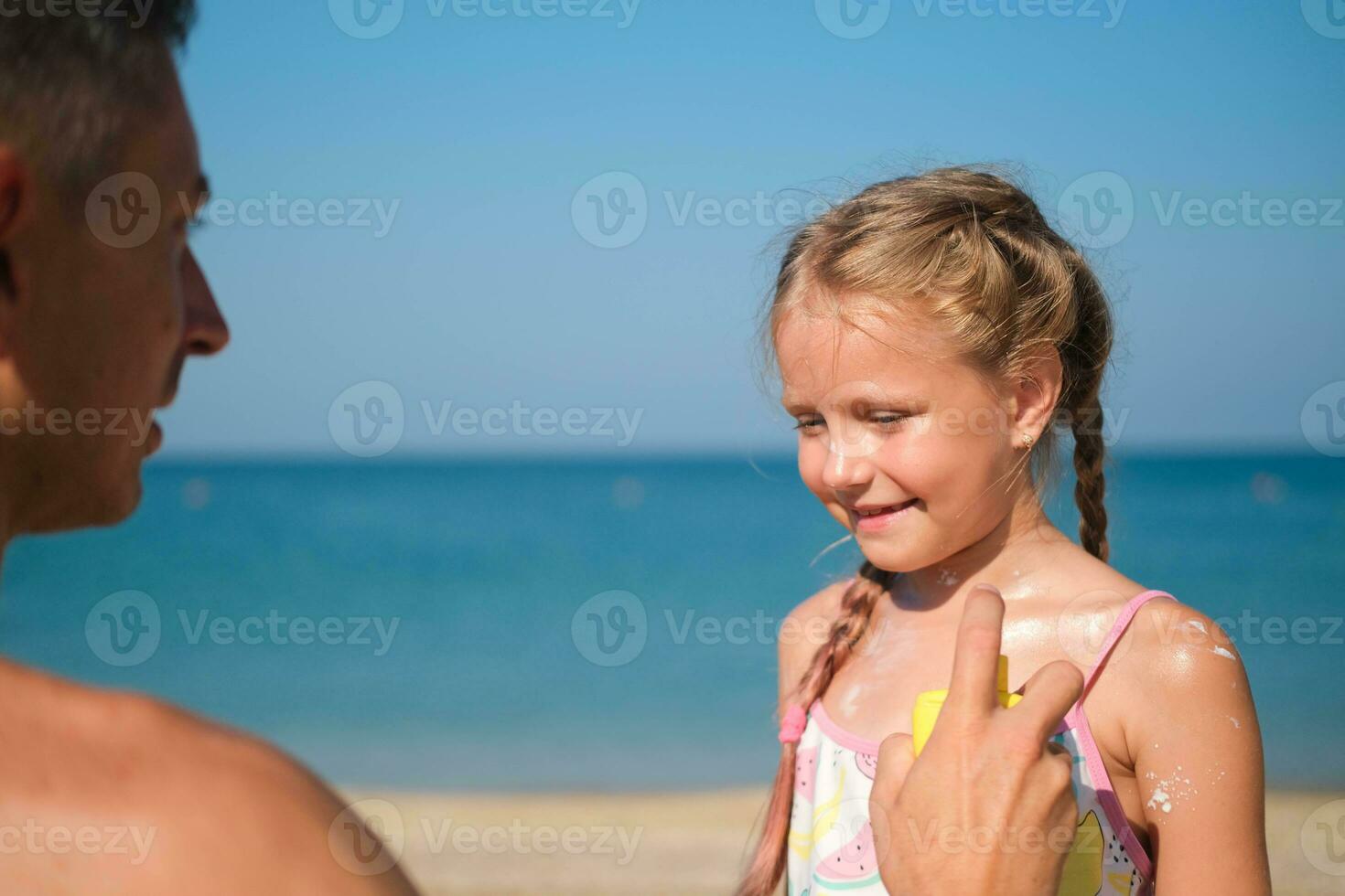 padre l'applicazione protettivo crema per sua di figlia viso a il spiaggia. uomo mano Tenere protezione solare lozione su bambino viso. carino poco ragazza con un' sole bloccare di il mare . copia spazio. foto