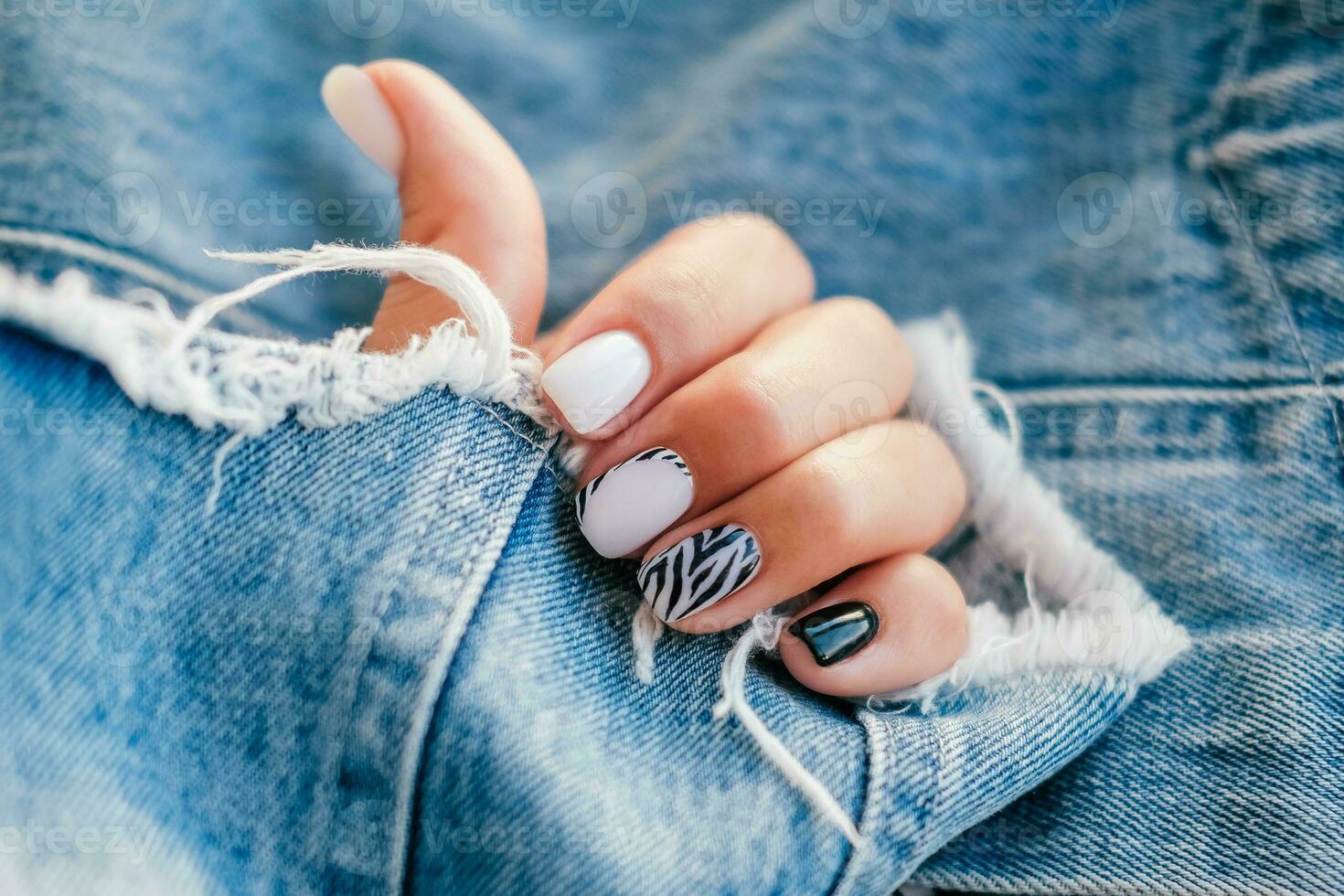 bellissimo femmina mani con manicure su il sfondo di denim. elegante chiodo design. manicure con nero e bianca zebra strisce su il chiodo. foto
