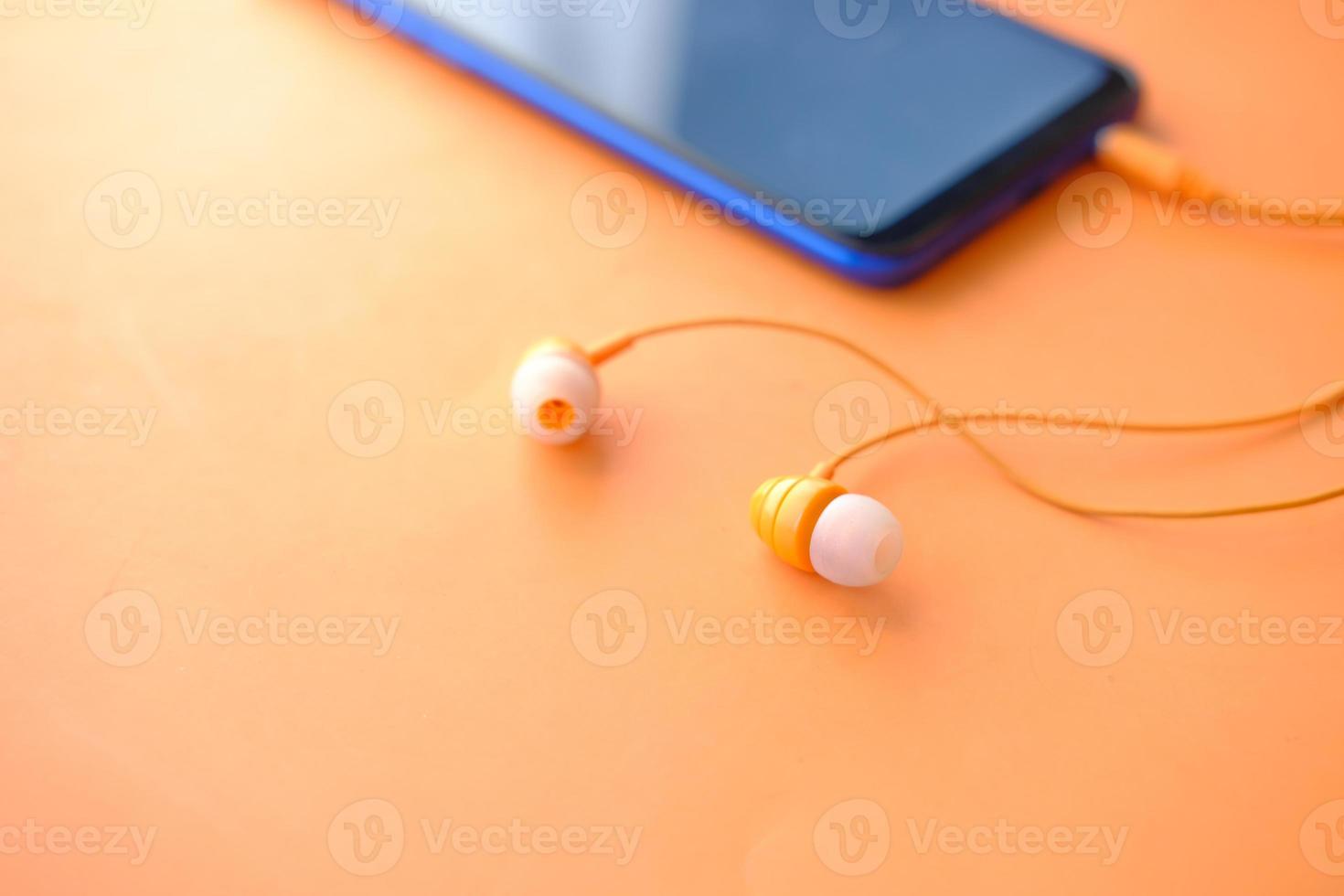 smartphone con schermo vuoto, auricolare su sfondo arancione foto
