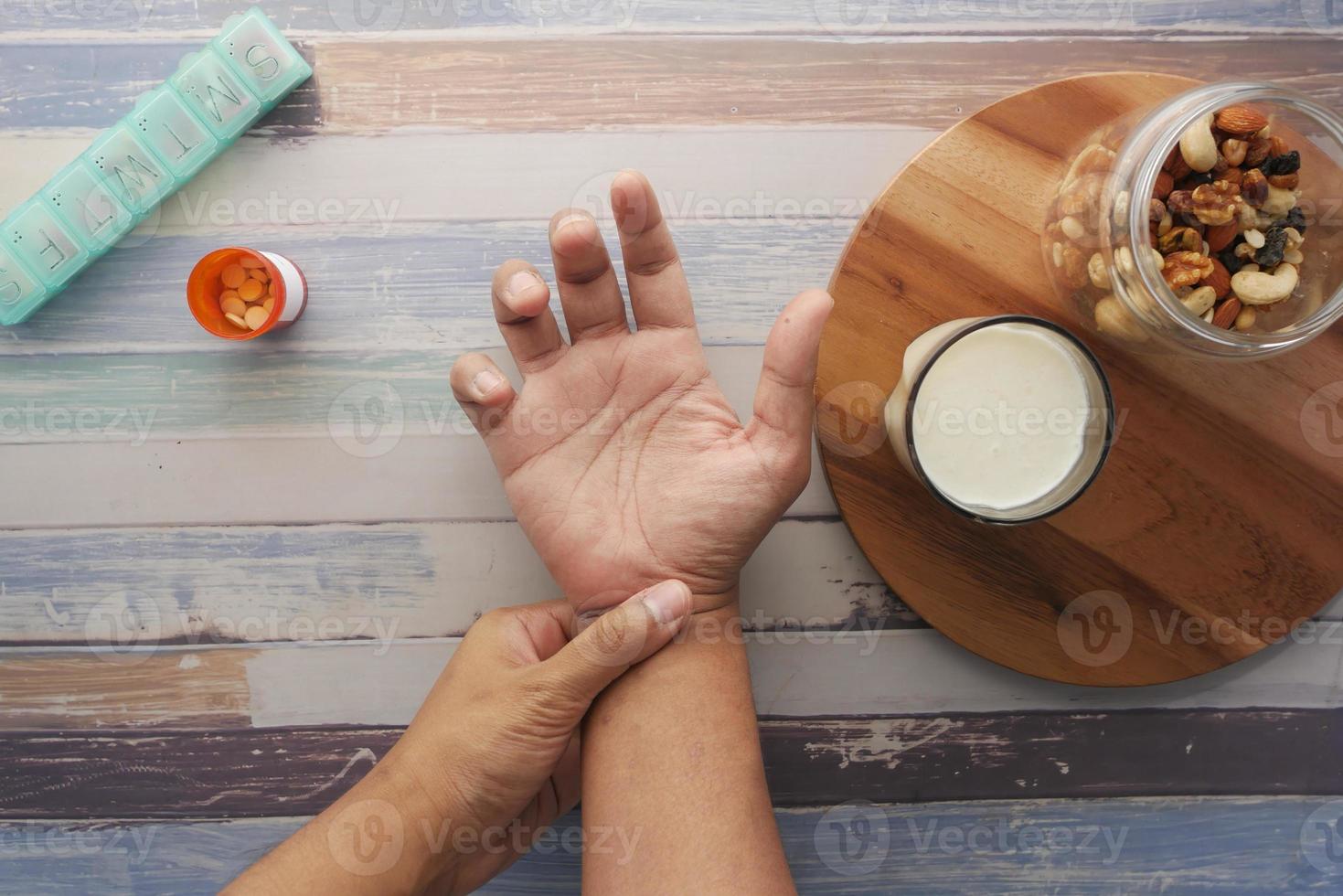 uomo che soffre di dolore alla mano con pillole mediche, latte e noci di mandorle sul tavolo foto