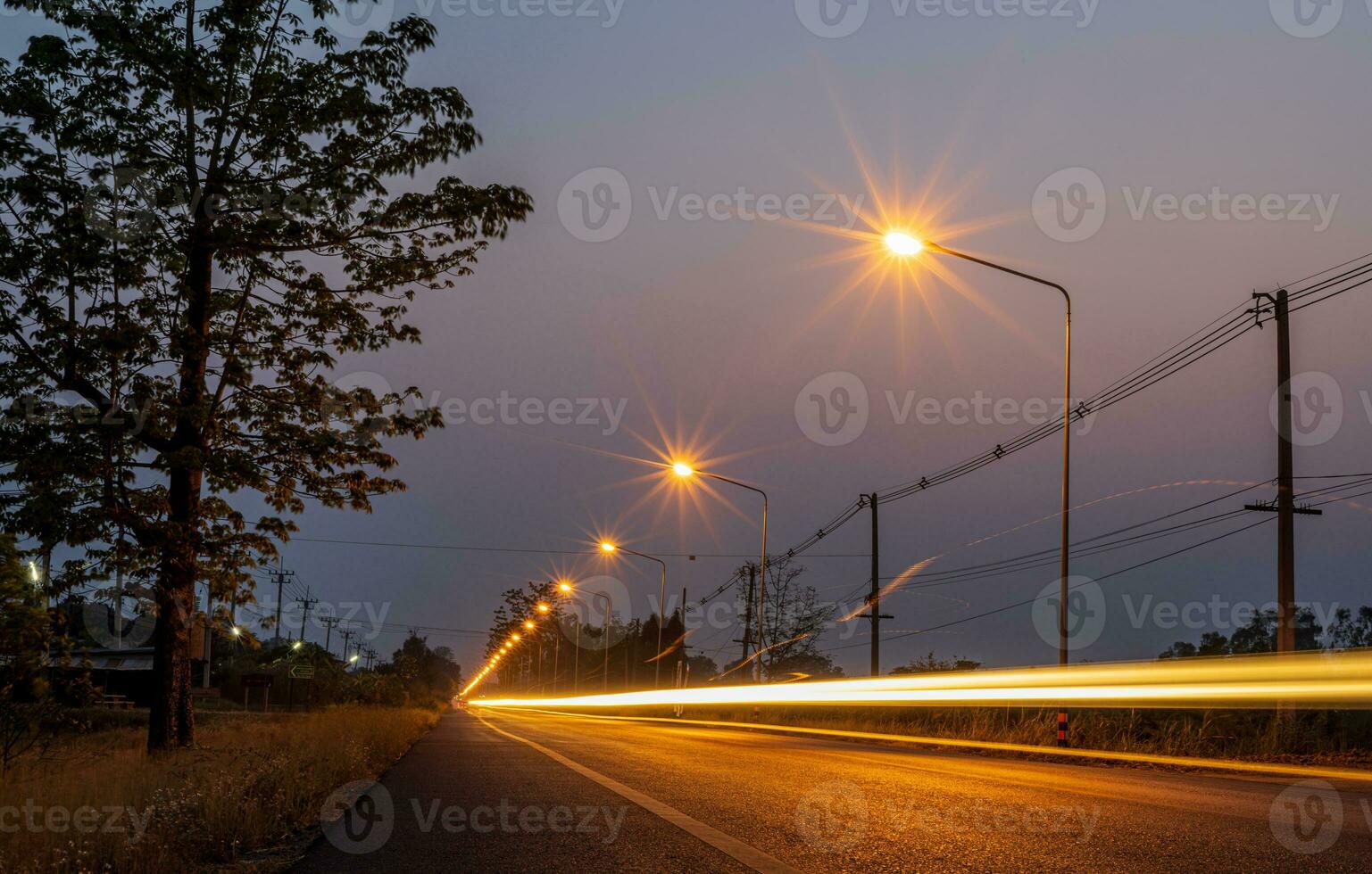 un' Visualizza di arancia esplosioni di stelle a partire dal un' lampione accanto un' strada con il leggero di un' passaggio macchina. foto