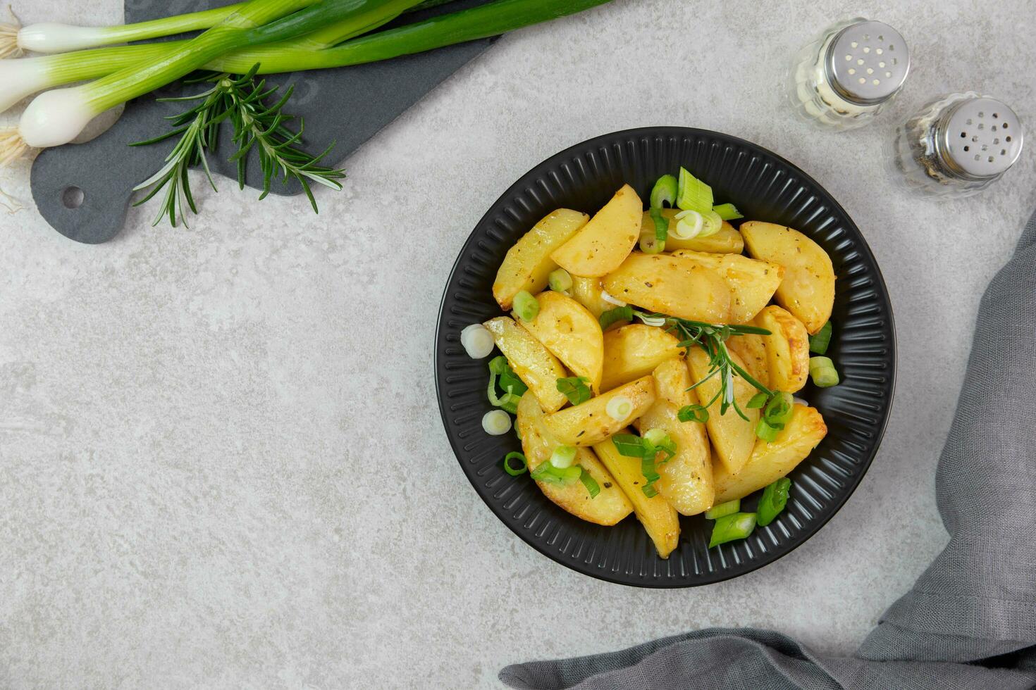 arrostito, al forno patate con fresco verde cipolle, Spezia e rosmarino su leggero grigio sfondo. superiore Visualizza. copia spazio. foto